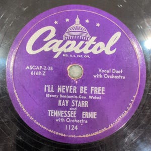 May include: A vintage vinyl record with a purple label featuring the Capitol Records logo and the text "I'll Never Be Free." The record features Kay Starr and Tennessee Ernie with an orchestra. The label also includes the number 1124.