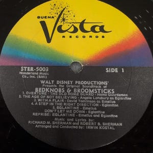 May include: A vintage vinyl record for the Walt Disney Productions soundtrack of "Bedknobs & Broomsticks." The label features a yellow and rainbow design with the Buena Vista Records logo. The tracklist includes songs like "The Age of Not Believing."