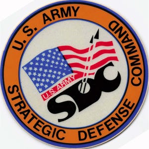 May include: Circular patch with an orange border and the text "U.S. ARMY STRATEGIC DEFENSE COMMAND". The center features the American flag and the letters "SBC" in black. The words "U.S. ARMY" are also present.