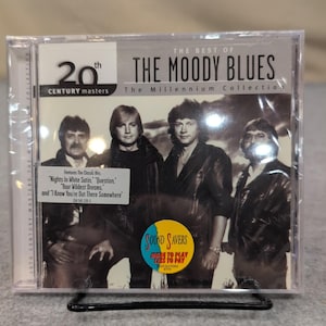 Peut inclure: Un boîtier de CD avec "The Best of The Moody Blues: The Millennium Collection." La pochette présente une photo en noir et blanc du groupe. Un autocollant indique "Sound Savers" et les titres des chansons.