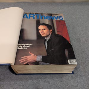 May include: A hardcover book with a blue spine and a magazine cover featuring a man in a black jacket. The magazine is titled "ARTnews" with the text "Brice Marden's Color-Coded Mysteries".