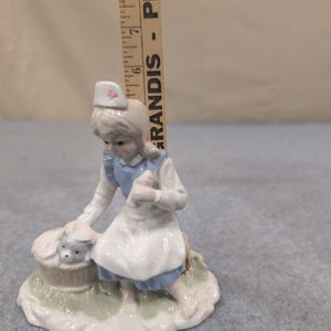 Statuetta vintage in porcellana raffigurante un'infermiera con un cucciolo in un cestino, nei colori blu e bianco. immagine 6