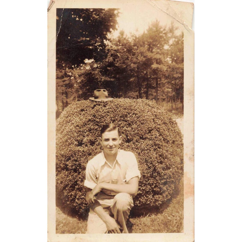 Fotografía vintage de los años 40 de un joven posando al aire libre con un sombrero y un arbusto. Retrato divertido. imagen 1