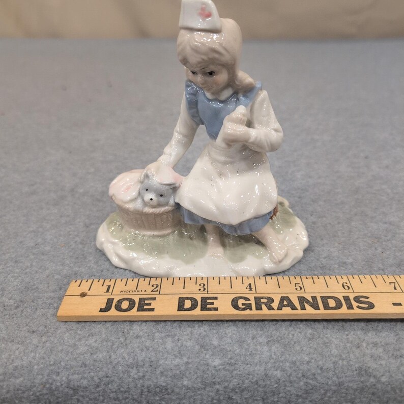 Statuetta vintage in porcellana raffigurante un'infermiera con un cucciolo in un cestino, nei colori blu e bianco. immagine 7