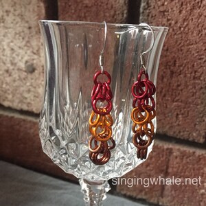 Może przedstawiać: Para kolczyków wiszących z gradientem kolorów: czerwonego, pomarańczowego i miedzianego. Kolczyki są wykonane z metalu i mają proste zapięcie na haczyk.