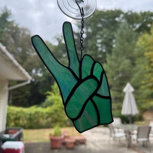 May include: A green stained glass peace sign hanging from a window with a suction cup.