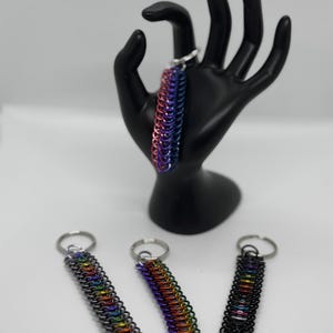 May include: Three rainbow colored chain keychains with silver key rings. The keychains are made of small metal rings that are linked together. The keychains are all different colors, but they all have a rainbow pattern.