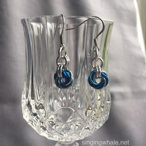 May include: A pair of silver earrings with blue and teal colored metal rings hanging from silver chains.