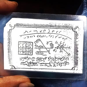 以下が含まれることがあります： 透明なプラスチック製のスリーブに入った、黒い文字と記号が書かれた白い長方形のカード。カードには複雑なパターン、幾何学的な形、手書きのスクリプトが表示されています。