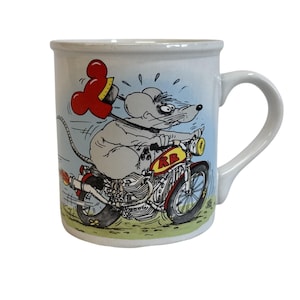 May include: White ceramic mug featuring a cartoon mouse riding a motorcycle. The mouse is gray with a surprised expression, holding a red object. The motorcycle is red and yellow, with the letters "RB" on the side. The background is light blue.