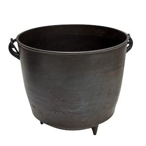May include: A dark gray cast iron cauldron with a rounded body, three short legs, and two side handles. The cauldron has a wide opening and a textured surface, suitable for cooking or decorative purposes.