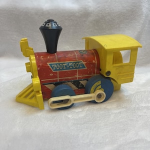 May include: A vintage toy train with a red body, yellow accents, and blue wheels. The train has the words "TOOT TOOT" printed on the side. The smokestack is black, and the train is made of wood and plastic.