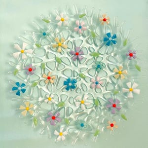 May include: A clear glass decorative plate with a floral design. The plate features a network of clear glass with colorful, small flowers in shades of yellow, pink, blue, and purple. Green leaves are interspersed among the flowers. The plate is round.