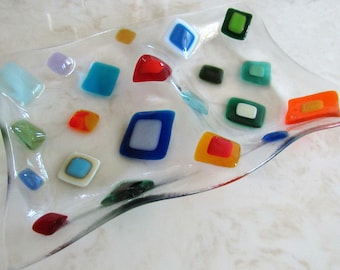 May include: A clear glass dish with a wavy edge, decorated with colorful glass squares in various shades of red, orange, yellow, green, blue, and purple.