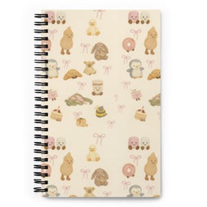 May include: Cream-coloured spiral-bound notebook with a repeating pattern of cartoon characters, including a duck, bunny, penguin, and bear, along with donuts, cakes, and bows. The notebook has a black spiral binding.