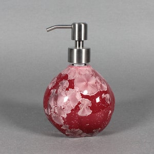 以下が含まれることがあります： ステンレス製のポンプが付いた、赤いセラミック製のソープディスペンサー。 ディスペンサーは丸い形で、薄いピンク色の花の模様で装飾されています。 ディスペンサーは液体石鹸用に設計されています。