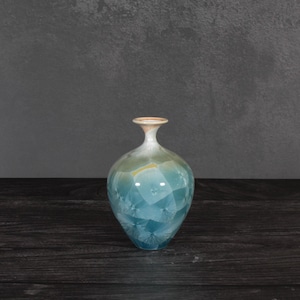 May include: A ceramic vase with a bulbous body and a narrow neck, featuring a crystalline glaze that transitions from a soft cream color at the rim to shades of blue and green across the surface, displaying star-like crystal formations throughout.