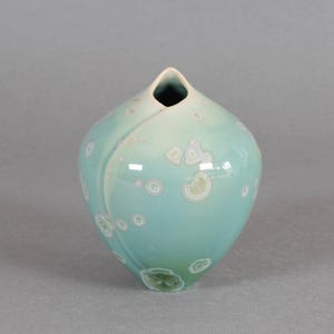 May include: A white ceramic mug with a black handle and the text "But First, Coffee" in a bold, black font. The mug is set against a blurred background, suggesting a cozy setting.