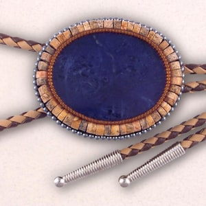 May include: A bolo tie with a blue stone set in a brown and beige beaded oval frame. The bolo tie has a brown and tan braided leather cord with silver metal tips.