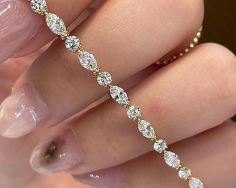 May include: A gold tennis bracelet featuring an alternating pattern of marquise-cut and round-cut clear gemstones. The stones are set in a continuous line, connected by small gold links, creating a delicate and shimmering piece of jewelry.