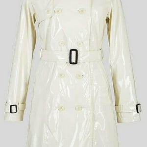 May include: A cream-colored trench coat with a glossy finish. The double-breasted coat features a belt, button details, and epaulettes. The coat has long sleeves and a classic collar.
