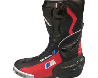 Puede incluir: Bota de moto negra y roja con el logo de BMW Motorrad. La bota presenta un diseño elegante con una raya roja y un protector de puntera plateado. El logotipo de Dainese es visible. Esta bota protectora está diseñada para montar en moto.