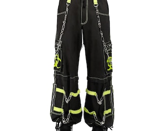 May include: Black cargo pants with neon green accents, white stitching, and silver chain details. The pants feature multiple pockets, zippers, and a biohazard symbol design. The pants are shown with black platform boots.