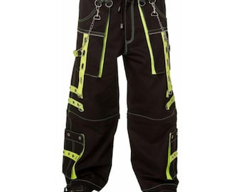 May include: Black cargo pants with neon green accents. The pants feature multiple pockets, straps, and chains. White stitching outlines the seams and neon green stripes. The pants have a drawstring waist and are worn with black shoes.