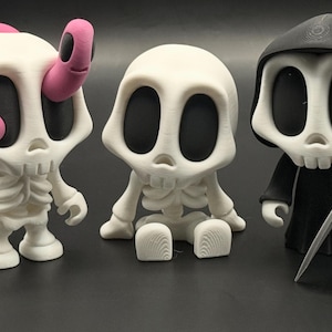 May include: Three white skeleton figurines with black eyes. One has pink horns, another is seated, and the third is dressed in a black robe and hood, holding a scythe. The figures have a cartoonish design.