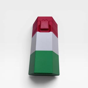 May include: A hexagonal container featuring a vertical color block design with a red top section, a white middle section, and a green bottom section. The top lid includes a small rectangular latch mechanism centered on the red panel.