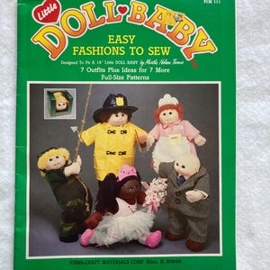 May include: A green sewing pattern booklet titled Little DOLL BABY Easy Fashions To Sew, designed for 14 inch dolls. The cover features seven outfits, including a yellow raincoat, a waitress uniform, a camouflage suit, and a formal suit.