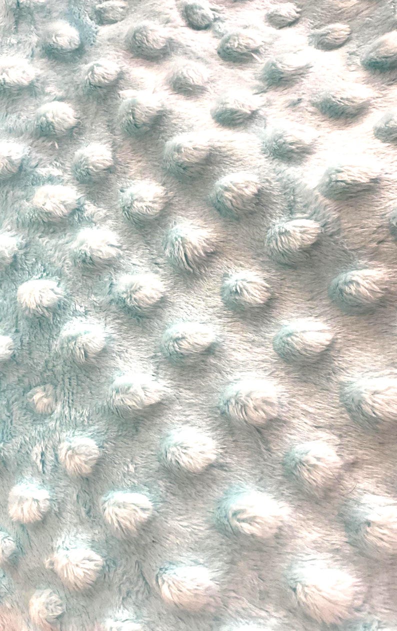 Puede incluir: Primer plano de una manta azul claro con una superficie texturizada. La manta tiene una textura suave y con bultos con mechones redondeados en relieve, creando una apariencia acogedora. La tela parece suave y c&aacute;lida.