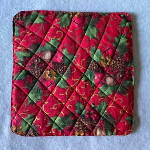 Può includere: Presina quadrata trapuntata a tema natalizio. Il cuscinetto presenta uno sfondo rosso con un motivo a rombi. Il motivo comprende foglie di agrifoglio verdi, pigne e accenti dorati. I bordi sono arrotondati.