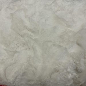 Puede incluir: Primer plano de una tela de piel sint&eacute;tica blanca, suave y texturizada. La tela tiene un patr&oacute;n ondulado, lo que le da un aspecto afelpado y lujoso. Ideal para mantas, mantas o ropa, el material es suave y acogedor.