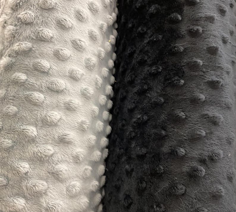 Puede incluir: Primer plano de dos rollos de tela de felpa. Un rollo es gris claro y el otro gris oscuro. Ambas telas tienen una superficie texturizada y con bultos, creando una apariencia suave y t&aacute;ctil. La tela probablemente se utiliza para mantas u otros art&iacute;culos acogedores.