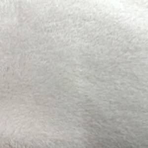 Puede incluir: Primer plano de una tela suave, blanca y esponjosa. La textura parece densa y afelpada, con una superficie ligeramente irregular. El material tiene un aspecto ligero y aireado, lo que sugiere un textil acogedor o delicado.