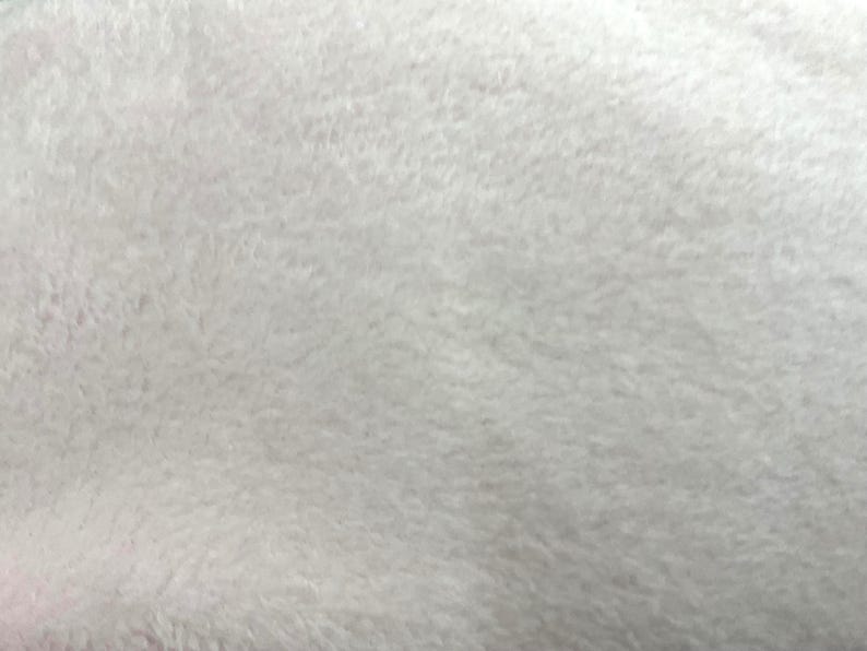 Puede incluir: Primer plano de una tela suave, blanca y esponjosa. La textura parece densa y afelpada, con una superficie ligeramente irregular. El material tiene un aspecto ligero y aireado, lo que sugiere un textil acogedor o delicado.