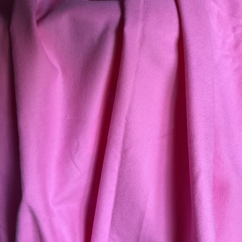 Puede incluir: Primer plano de una tela rosa vibrante con pliegues suaves y sombras sutiles. El material parece liso, posiblemente un textil de peso medio, adecuado para proyectos de ropa o decoraci&oacute;n del hogar.
