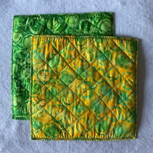 Peut inclure: Deux dessous de plat carrés matelassés. L'un est vert uni avec un motif circulaire. L'autre est jaune et vert avec un motif en losange. Les deux ont un bord cousu décoratif. Les dessous de plat sont probablement destinés à la cuisine.
