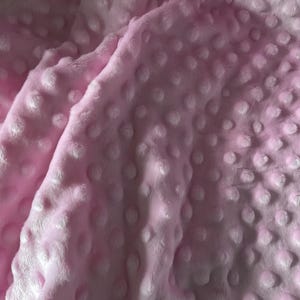 Puede incluir: Primer plano de una manta rosa suave con una superficie texturizada. La manta tiene un patr&oacute;n de hoyuelos, creando una apariencia afelpada y acogedora. La tela est&aacute; doblada, mostrando la profundidad y textura del material.