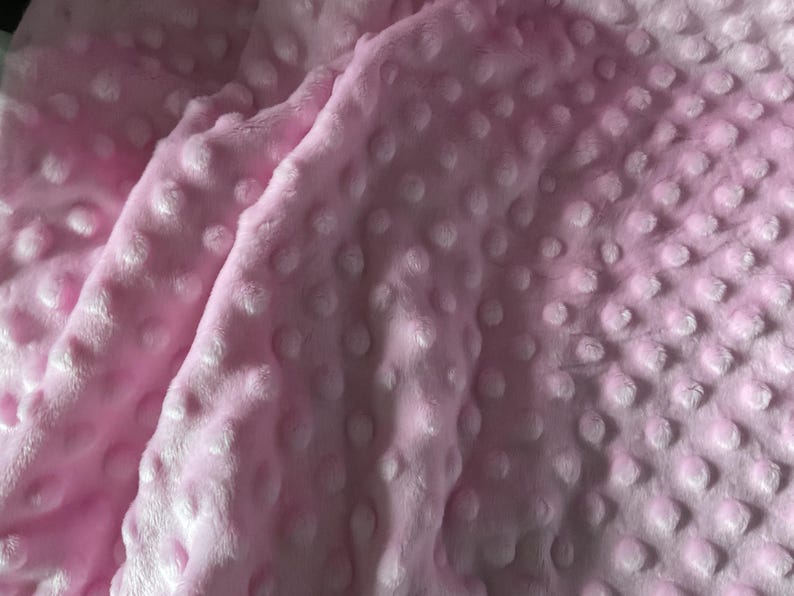 Puede incluir: Primer plano de una manta rosa suave con una superficie texturizada. La manta tiene un patr&oacute;n de hoyuelos, creando una apariencia afelpada y acogedora. La tela est&aacute; doblada, mostrando la profundidad y textura del material.
