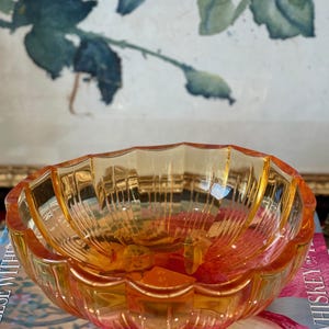May include: A translucent amber-colored glass bowl with a scalloped rim and vertical ribbed detailing along the interior walls. The bowl features a rounded, multi-faceted design that catches light, creating a warm, glowing appearance throughout the glass.