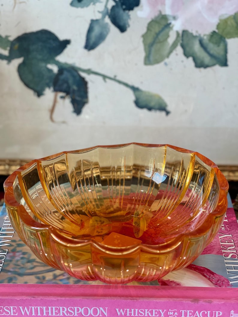 May include: A translucent amber-colored glass bowl with a scalloped rim and vertical ribbed detailing along the interior walls. The bowl features a rounded, multi-faceted design that catches light, creating a warm, glowing appearance throughout the glass.