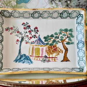 May include: A rectangular ceramic serving tray with bamboo-style handles and edges. The white interior features a hand-painted scene of a pagoda, a flowering tree with red blossoms, and a pine tree. A green geometric lattice pattern borders the rim.