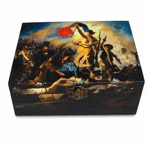 May include: A rectangular wooden box featuring a reproduction of the painting Liberty Leading the People on its lid. The box has a dark finish and a metallic latch on the front. The artwork depicts a group of figures with a French flag.