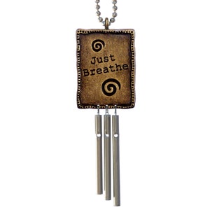 May include: A gold-toned metal pendant with the words "Just Breathe" and a swirl design. The pendant is attached to a silver chain and has five silver chimes hanging from it.