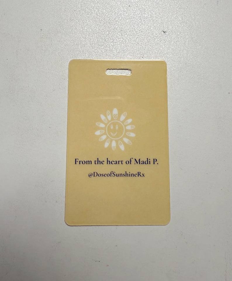 May include: A rectangular, pale yellow card with a hole at the top. It features a white smiling sun graphic and the text "From the heart of Madi P. @DoseofSunshineRx".