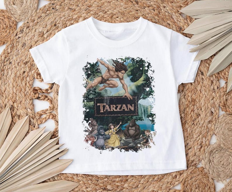 May include: White t-shirt featuring a colorful graphic of Tarzan jumping, with the word "Tarzan" on a sign. The design includes jungle elements and various characters from the animated movie.