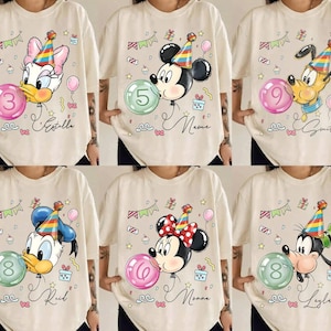 May include: A collection of six beige t-shirts, each featuring a different Disney character wearing a colorful party hat and blowing a bubble with a number inside. The designs include party decorations like balloons, bunting, and gifts, with a name written below.