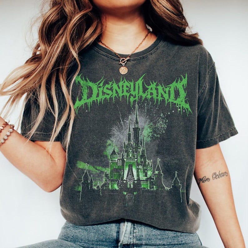 Puede incluir: Camiseta gris oscuro con un dise&ntilde;o verde de un castillo y la palabra "Disneyland" en una fuente desgastada. El dise&ntilde;o incluye fuegos artificiales y una silueta de castillo. La camiseta tiene un aspecto vintage.